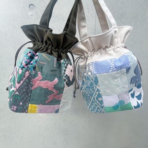 May include: Two drawstring tote bags with patchwork designs. One bag has a green handle and a patchwork of pink, green, and white fabrics with a rabbit motif. The other bag has a beige handle and a blue and white patchwork design.