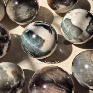 May include: A set of three ceramic mugs with a speckled, cream-coloured glaze. Each mug features a different hand-painted design: a sun, a moon, and a star. The mugs have a simple, modern design with a rounded shape.