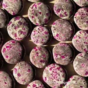 May include: A collection of round, polished stones with a speckled appearance. The stones are primarily gray with vibrant pink and magenta inclusions. The arrangement suggests a focus on natural gemstones or decorative elements.