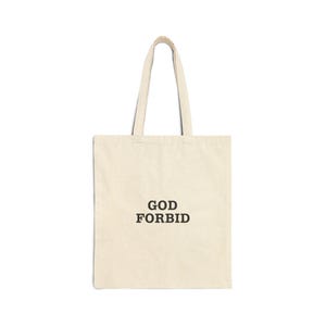 May include: Cream-colored tote bag with the words "GOD FORBID" printed in black, centered on the front. The bag has two matching handles for carrying. The bag is made of a sturdy fabric.
