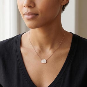 Könnte beinhalten: Eine zarte goldene Halskette mit einem wolkenförmigen Anhänger, der mit kleinen, funkelnden Steinen besetzt ist. Der Anhänger ist an einer feinen Kette befestigt und schafft ein minimalistisches und elegantes Design. Die Halskette wird über einem schwarzen Oberteil getragen.