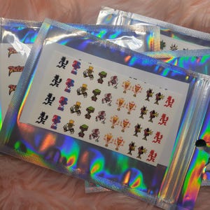 May include: Several holographic pouches containing sticker sheets. The sticker sheets feature various cartoon characters in different colors. One sheet has the word "Twisted" printed on it. The pouches are sealed with a clear plastic closure.