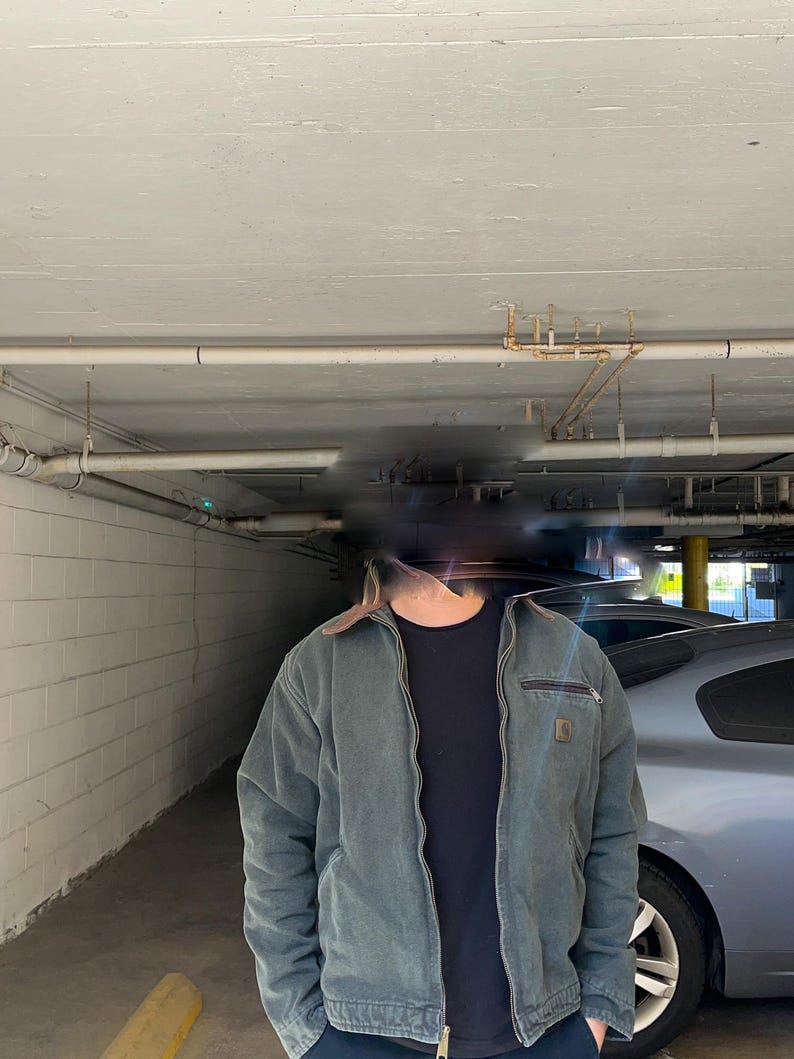 Pu&ograve; includere: Giacca da lavoro color verde acqua con colletto marrone e chiusura a zip. La giacca presenta un piccolo logo quadrato sul petto e una tasca con zip sulla parte superiore sinistra. Sotto &egrave; indossata una maglietta nera.