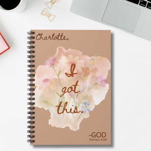Könnte beinhalten: Spiralgebundenes Notizbuch mit braunem Einband, floralem Aquarelldesign und dem Text "I got this". Der Name "Charlotte" steht oben. Unten steht der Text "-GOD (Römer 8,28)."
