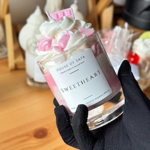 Op de afbeelding: Een glazen kaars gevuld met roze was, getopt met witte opgeklopte was en roze hartvormige wasdecoraties, met een klein roze chocoladereep-accent. Het etiket leest HOUSE OF SAFA, Handcrafted in Amsterdam, SWEETHEART, 100% coconut-soywax | 250g.