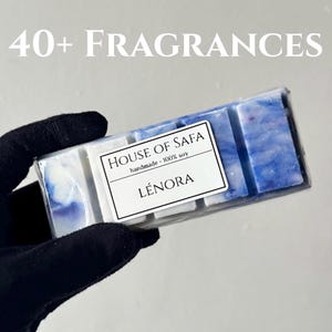 Peut inclure: Une tablette de cire parfumée rectangulaire au motif marbré bleu et blanc, emballée dans du plastique transparent. Une étiquette blanche indique : 40+ FRAGRANCES, HOUSE OF SAFA, handmade - 100% soy, LÉNORA. La tablette est divisée en cinq segments.