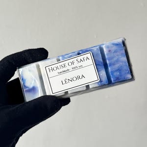 Op de afbeelding: Een rechthoekige wax melt bar met een gemarmerd blauw en wit patroon. Een wit label is in het midden aan de voorzijde geplaatst, met de tekst HOUSE OF SAFA, handmade - 100% soy, en LÉNORA in zwarte letters. De wax is verdeeld in vijf blokjes.