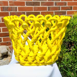 Peut inclure: Un panier en céramique jaune vif présentant un motif en treillis décoratif avec une texture rappelant une corde tressée. Le récipient possède un large sommet ouvert avec un bord festonné et une base plate et solide, avec une finition brillante.