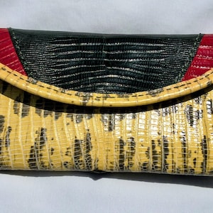 May include: A rectangular wallet featuring a textured yellow and black lizard-skin pattern. The flap closure is accented with a dark green centre panel and red side panels, all displaying a consistent, fine-grained, reptilian-inspired texture.