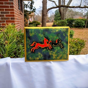 May include: A rectangular canvas art piece featuring two horses. One horse is red with a yellow outline, and the other is black. The background is a mix of green and black, with a gold border.
