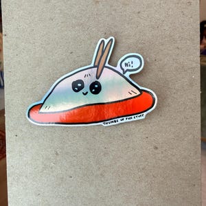 May include: A sticker featuring a cartoon alien in a red saucer with the text "Thumbs Up Fun Stuff." The alien has large black eyes, a smiling mouth, and two antennae. A speech bubble says "Hi!"