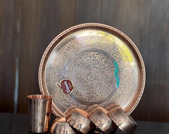 Puede incluir: Un juego de servir de color cobre con una bandeja grande y redonda con intrincados diseños florales. El juego incluye cuencos pequeños, tazas y cucharas, todos con diseños a juego. La bandeja tiene un borde decorativo.