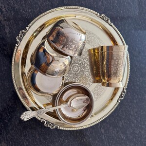 Puede incluir: Una bandeja dorada con detalles ornamentados contiene varios cuencos, tazas y una cuchara peque&ntilde;os de plata. La bandeja tiene un dise&ntilde;o floral en el centro y un borde decorativo. El juego incluye cuatro cuencos peque&ntilde;os, dos tazas y un cuenco peque&ntilde;o con una cuchara.