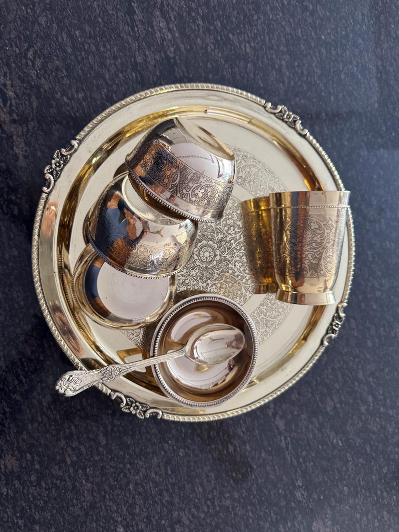 Puede incluir: Una bandeja dorada con detalles ornamentados contiene varios cuencos, tazas y una cuchara peque&ntilde;os de plata. La bandeja tiene un dise&ntilde;o floral en el centro y un borde decorativo. El juego incluye cuatro cuencos peque&ntilde;os, dos tazas y un cuenco peque&ntilde;o con una cuchara.