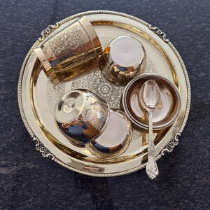 Puede incluir: Un juego de servir de metal dorado sobre una bandeja redonda. El juego incluye una taza alta con dise&ntilde;os florales grabados, dos tazas peque&ntilde;as, un cuenco peque&ntilde;o con una cuchara y dos tapas. La bandeja y el juego tienen detalles ornamentados.