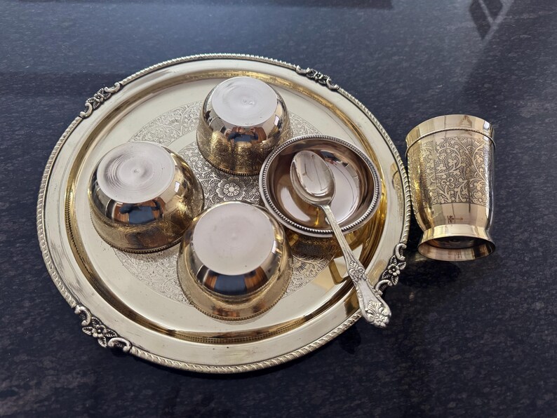 Puede incluir: Un juego de servir dorado con una bandeja decorativa, cuencos peque&ntilde;os y una taza. La bandeja tiene un borde adornado y contiene tres cuencos peque&ntilde;os, un cuenco peque&ntilde;o con una cuchara y una taza con dise&ntilde;os grabados. El juego es probablemente para servir comida o bebidas.