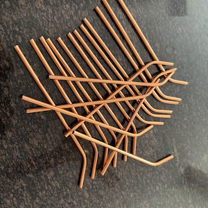 Può includere: Una scultura in filo di rame con un design intrecciato. La scultura è realizzata con fili di rame sottili e dritti che sono piegati e intrecciati per creare una forma astratta unica. Il rame ha un colore marrone-rossastro caldo.