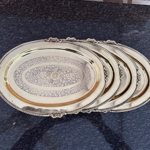 Puede incluir: Juego de cinco bandejas ovaladas con diseños florales y de volutas ornamentadas. Las bandejas tienen un acabado dorado y bordes decorativos. El centro de cada bandeja presenta un patrón floral ovalado.