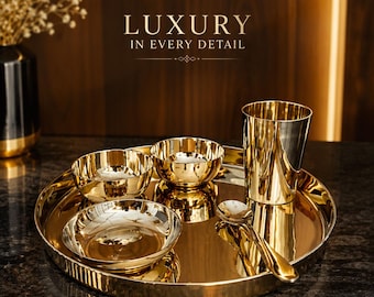 Puede incluir: Un juego de vajilla de color dorado pulido que incluye una bandeja redonda grande, dos cuencos pequeños, un plato hondo, un vaso alto y una cuchara. El texto LUXURY IN EVERY DETAIL aparece sobre el conjunto dispuesto en una superficie oscura.