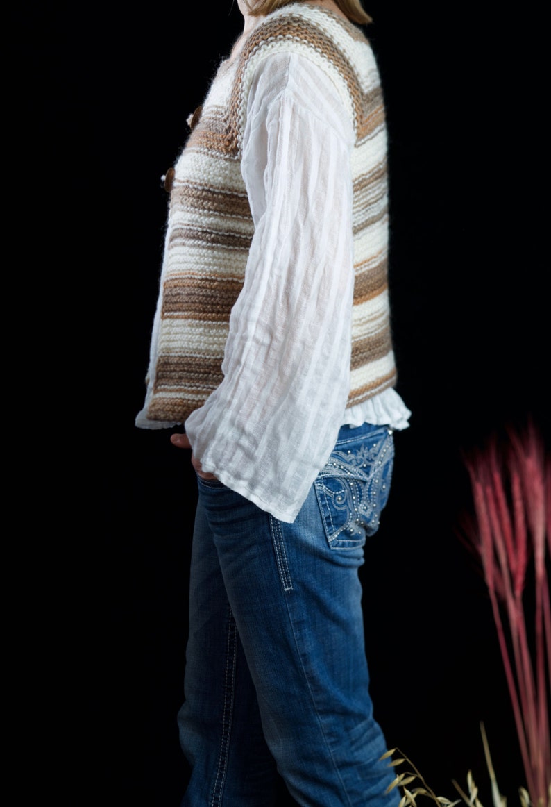 May include: A woman wearing a brown and white striped knitted vest over a white blouse and blue jeans with rhinestone detailing.