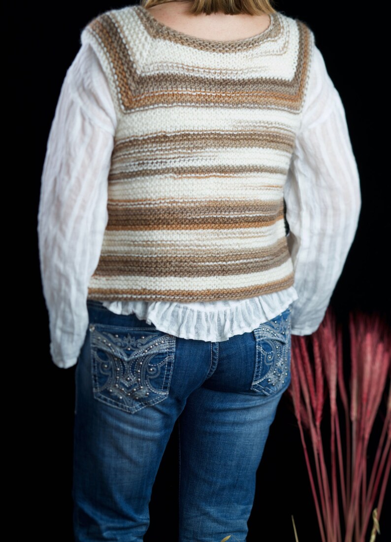 May include: A white and brown striped knitted vest with a ruffled white shirt underneath and blue jeans with embellished pockets.