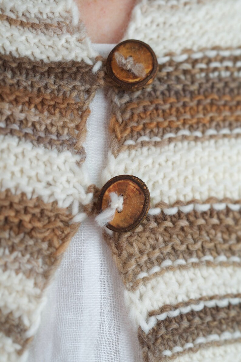 May include: A close-up of a brown and white striped knitted cardigan with two wooden buttons.