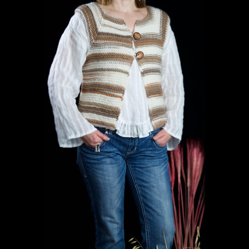 May include: A woman wearing a striped knitted vest with brown and white stripes and two wooden buttons. She is also wearing a white blouse and blue jeans.