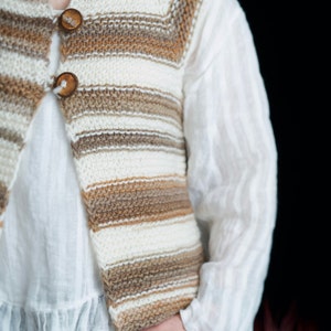 May include: A striped knitted vest with brown and white stripes. The vest has a V-neck and two wooden buttons.