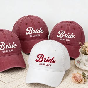 Könnte beinhalten: Drei kastanienbraune Baseballkappen und eine weiße Baseballkappe, jeweils mit dem gestickten Wort Bride in Schreibschrift, gefolgt vom Datum 06-05-2026. Die kastanienbraunen Kappen haben weißen Text, die weiße Kappe hat kastanienbraunen Text.