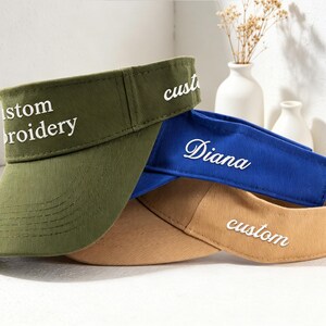 May include: Three visors in olive green, blue, and tan. The olive green visor has "custom embroidery" embroidered in white. The blue visor has "Diana" embroidered in white. The tan visor has "custom" embroidered in white.