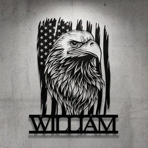May include: Black metal wall art featuring an eagle's head against a backdrop of the American flag. The eagle is intricately detailed. The name "WILLIAM" is displayed below the eagle in bold, capital letters.
