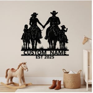 May include: A black metal wall art piece featuring a silhouette of a family of four riding horses. The design includes two adults and two children, with the text CUSTOM NAME and EST 2025 displayed in a bold, sans-serif font at the bottom.