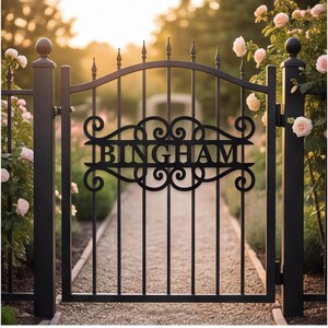 以下が含まれることがあります： 中央の水平パネルに大文字で「BINGHAM」と記された黒い金属製のガーデンゲート。ゲートには垂直の格子、先端が尖ったアーチ状の上部レール、そしてネームプレートを囲む装飾的なスクロール模様が施されています。