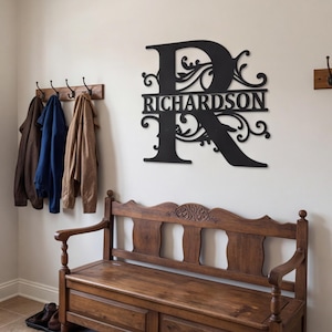 Puede incluir: Un letrero de pared de metal negro que presenta una letra R mayúscula grande con patrones de volutas intrincados y el nombre RICHARDSON centrado horizontalmente en la letra, montado en una pared lisa sobre un banco de madera con percheros.