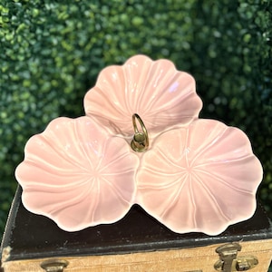 Puede incluir: Un plato para servir de color rosa claro con tres secciones y un asa dorada. El plato tiene un borde festoneado y un diseño floral en cada sección. El plato para servir es de cerámica.