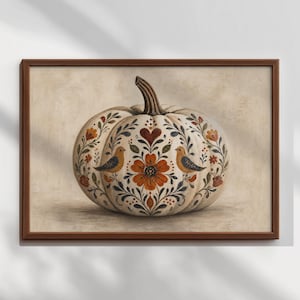 May include: A framed wall art print featuring a cream-coloured pumpkin decorated with intricate folk-style floral patterns, dark blue leaves, and two small birds facing a central orange flower, all enclosed in a simple dark brown wooden frame.