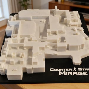 May include: A white 3D-printed model of the "Mirage" map from the video game Counter-Strike. The model is set on a black base, with the game's logo in white text. The map features detailed architectural elements.