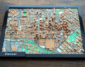 May include: A framed 3D map of Denver, Colorado, showing a detailed representation of the city's layout. The map is in shades of brown and green, with a black frame and the city name on a small black plaque.