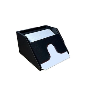 May include: A black, angled napkin holder with a white cutout on the front. The holder is filled with a stack of white napkins. The design is simple and modern, suitable for a kitchen or dining area.