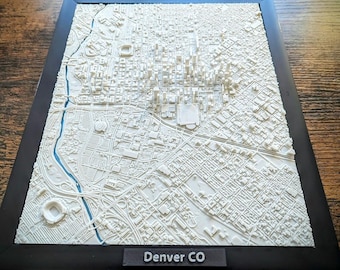 May include: A 3D relief map of Denver, Colorado, framed in black. The map is white, showing the city's layout with detailed streets, buildings, and a blue river. The text "Denver CO" is at the bottom.