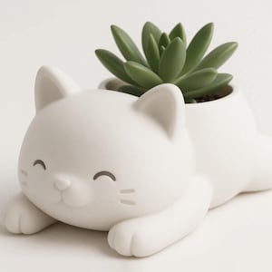 Puede incluir: Una maceta blanca de cerámica con forma de gato y una planta suculenta. La maceta tiene una cara sonriente, patas y orejas. La suculenta tiene hojas verdes. Un artículo decorativo para el hogar o la oficina.