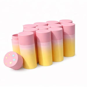 Op de afbeelding: Een verzameling roze en gele cilindrische containers met roze deksels. Eén container ligt op zijn kant en toont een sterrenontwerp. De containers hebben een kleurenschema met een verloop, dat overgaat van roze naar geel.