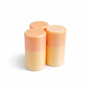 Op de afbeelding: Drie cilindrische containers, elk met een tweekleurig ontwerp. Het bovenste gedeelte is licht perzik van kleur, terwijl de onderkant zachtgeel is. De containers zijn in een cluster gerangschikt, wat wijst op een set of collectie.