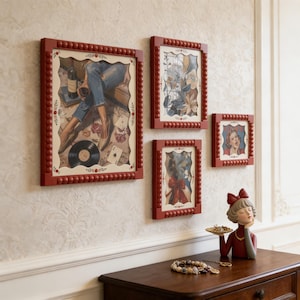 May include: A set of framed art prints with red beaded frames, showcasing diverse illustrations. A decorative figurine in a red dress holding a tray of jewellery sits on a wooden table. A necklace and other jewellery are also on the table.