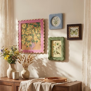 May include: A gallery wall arrangement featuring a large pink scalloped frame with a yellow floral print, a light blue rounded frame with a botanical print, a dark brown scalloped frame with a butterfly print, and a green scalloped frame with butterflies.