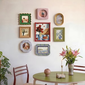 May include: A selection of framed art pieces in diverse shapes and colours, including green, red, and gold. The frames feature unique details, such as scalloped edges and beaded borders. The artwork within the frames depicts scenes of flowers, still life arrangements, and landscapes.