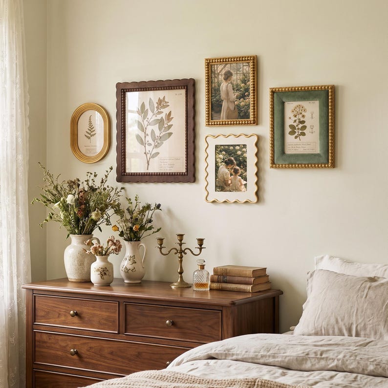 May include: A collection of four wall-mounted picture frames in various shapes and colors, including gold, dark brown, and green, displaying botanical prints and photographs. The frames are arranged above a wooden dresser with vases and a candle holder.