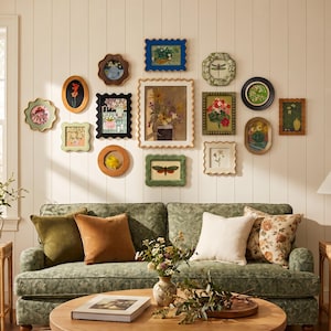 May include: A gallery wall featuring a collection of various framed art pieces with floral, insect, and botanical illustrations in diverse shapes and colours, arranged above a green patterned sofa with four solid and floral throw pillows.