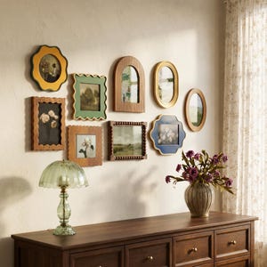 May include: A gallery wall arrangement featuring nine diverse picture frames in various shapes, including scalloped, arched, and oval designs, finished in wood, gold, yellow, green, and blue tones, displayed above a wooden dresser with a lamp.