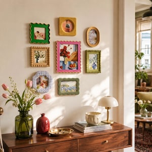 Puede incluir: Una colección de siete marcos de fotos montados en la pared de diversas formas, colores y texturas, incluyendo bordes festoneados, con cuentas y lisos. Los marcos muestran impresiones artísticas variadas y están dispuestos sobre una mesa consola.